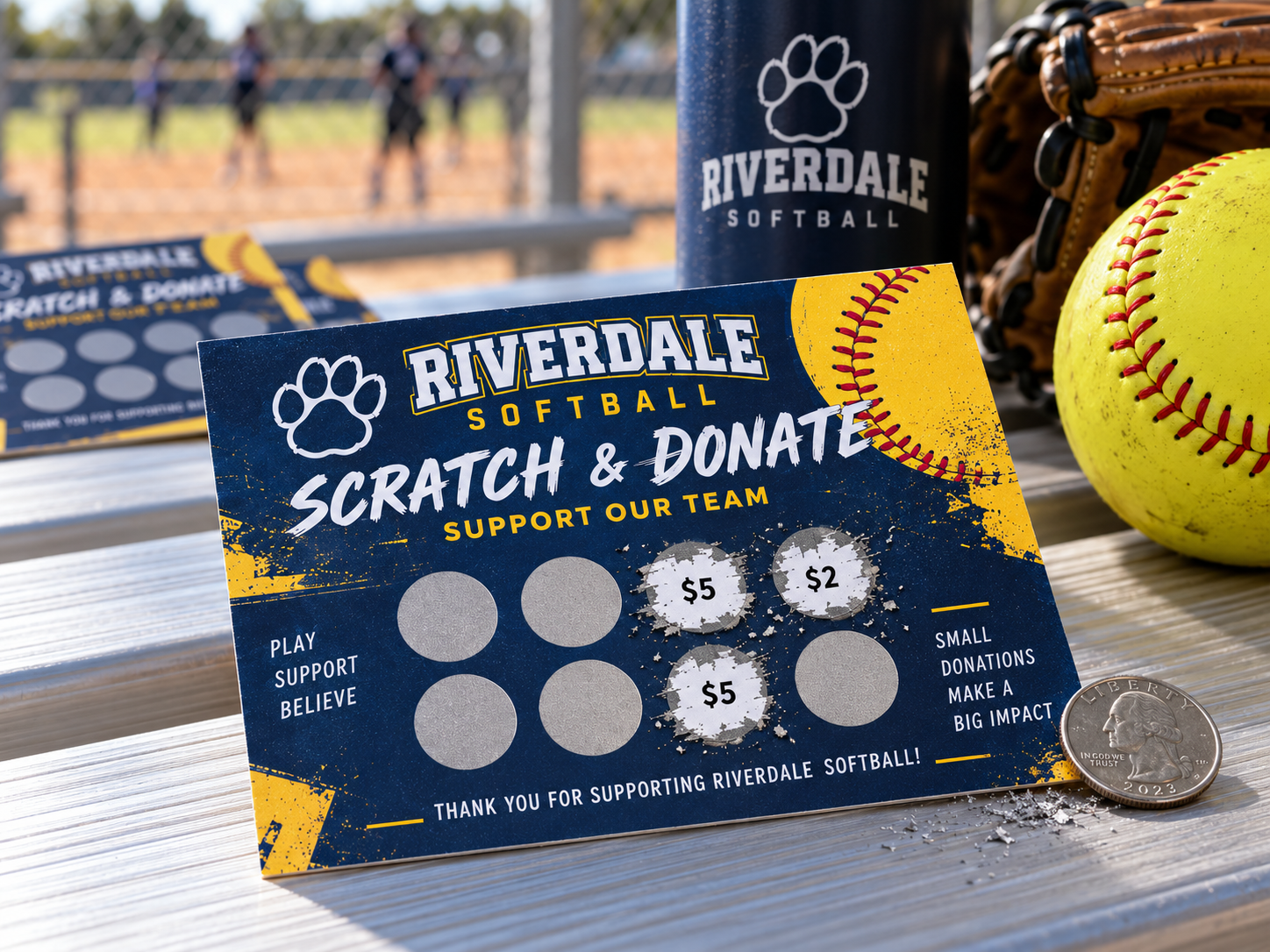 Navy and gold softball team scratch and donate fundraising card standing on aluminum bleachers with revealed $5 and $2 donation amounts, a quarter, softball, and glove